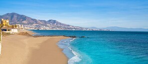 Une plage à l’eau d’un bleu limpide, avec une côte rocheuse et une montagne en arrière-plan.