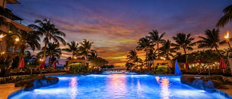Ein Swimmingpool mit Sonnenuntergangsblick, umgeben von Palmen und Hotelgebäuden.
