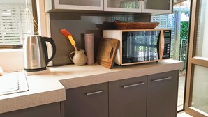 A kitchen with a microwave, kettle, and wooden cutting board on the counter.