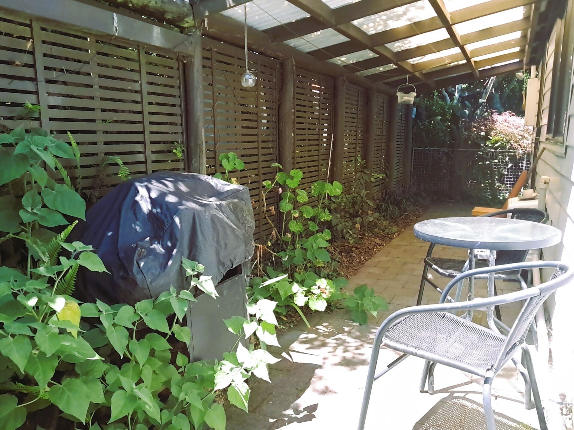 Ein überdachter Patio-Bereich mit Grill, Tisch und Stühlen.
