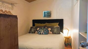 Een slaapkamer met een bed, nachtkastje, lamp, kledingkast en een wandplank.