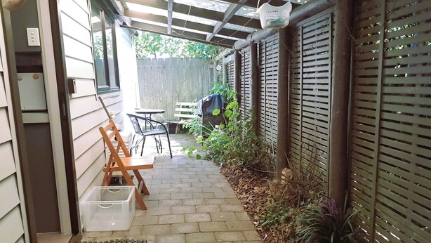 A narrow brick pathway leading to a patio area with a wooden bench, a table, and chairs.