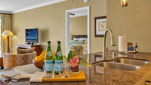 A hotel kitchen with a granite countertop, a sink, a dining area with a chair, a television, and a decorative vase with flowers. - Honua Kai | Ocean View 6 BR, Sleeps 20 | Car Incl. w/ 6+ Nights | HKK ML-3571 by KBM (Lahaina)