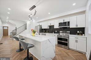 Una cocina moderna con armarios blancos, una isla de mármol y electrodomésticos de acero inoxidable.