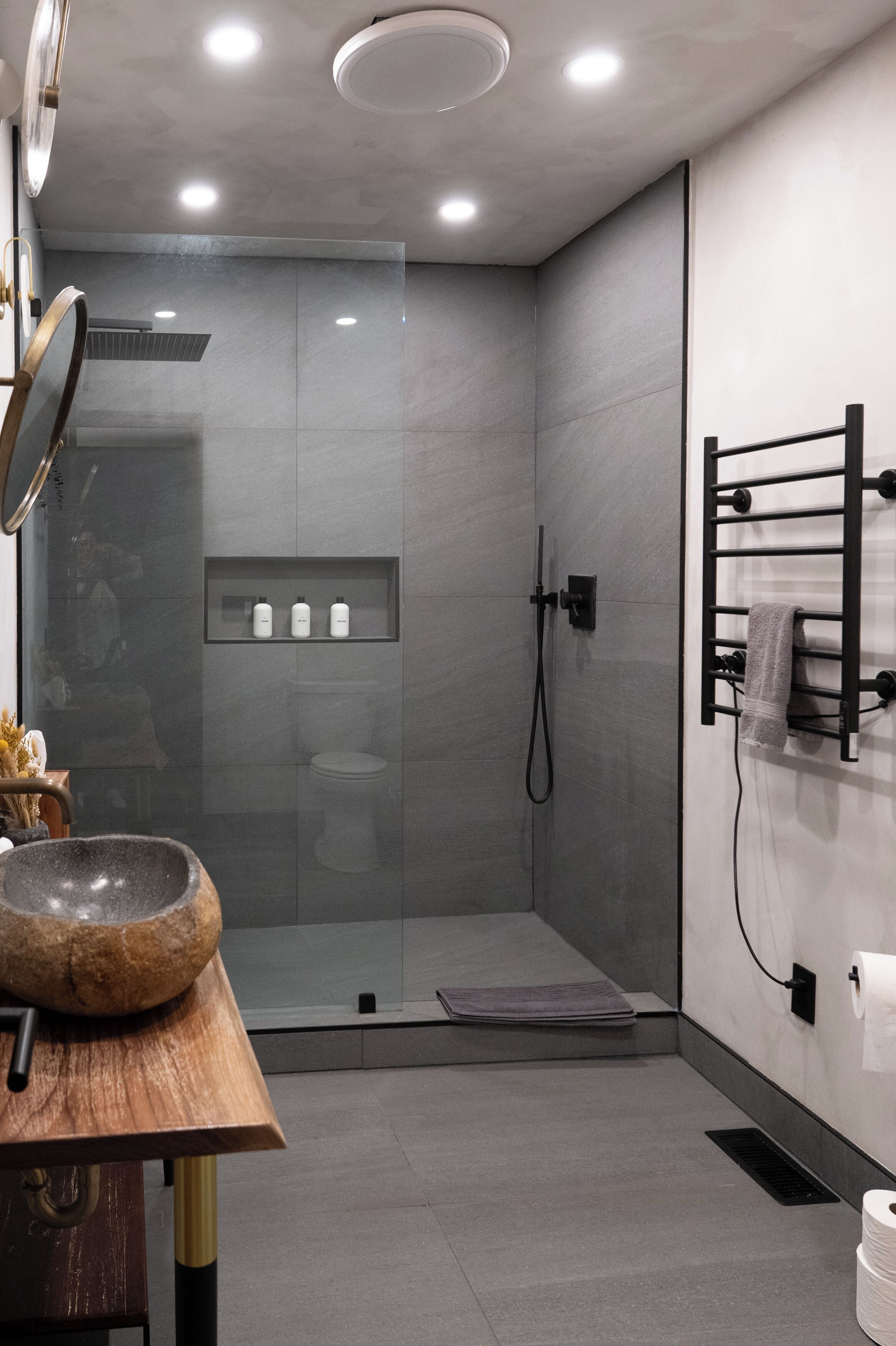 A modern bathroom with a glass shower enclosure, a wooden vanity with a bowl sink, and a towel rack.