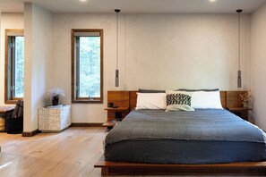 Ein modernes Schlafzimmer mit einem großen Bett, einem Holzkopfstück und Blick auf Bäume durch ein Fenster.
