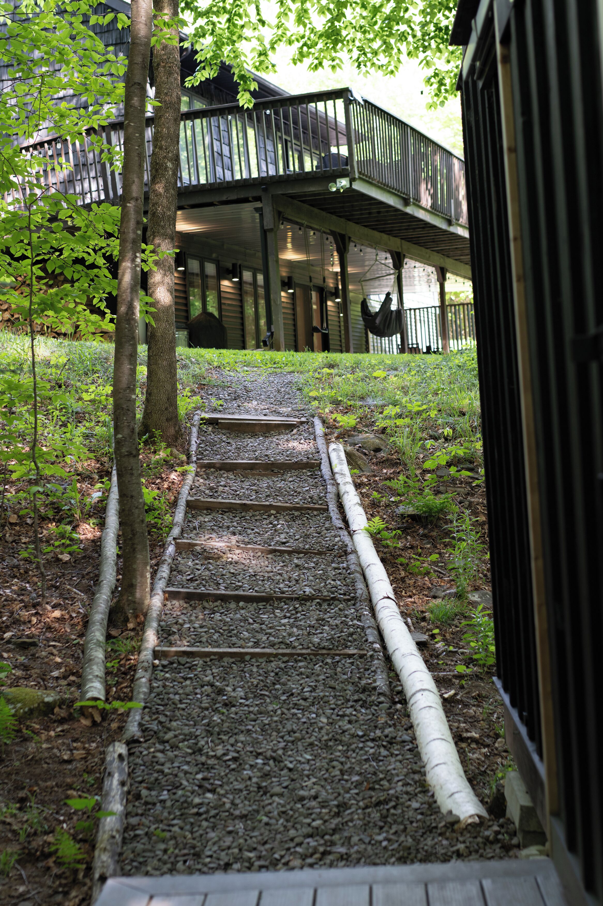 A pathway leading to a wooden structure with a balcony, surrounded by trees and greenery.