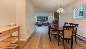 Ein Essbereich mit Holztisch und Stühlen, einer Chandelierleuchtre und Blick auf ein Wohnzimmer mit Sofa und Fernseher.