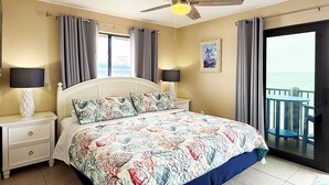Un dormitorio con cama, mesitas de noche, ventilador de techo y vista al océano a través de una puerta corredera.