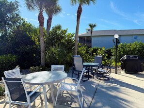 An outdoor patio with a round table and chairs, surrounded by palm trees and a house in the background. - Sea Oats 1BR Condo – Pool, Beach, Boat Slip (Englewood)