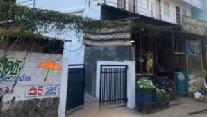 Un immeuble à plusieurs étages, doté d’une entrée sécurisée par un portail et abritant une petite boutique vendant des légumes.