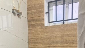Une petite salle de bain compacte, avec des toilettes blanches, un espace douche et une fenêtre.