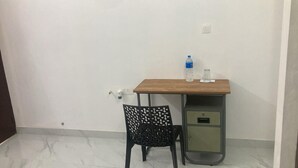 Un petit bureau avec un bureau en bois, une chaise noire à motifs originaux, une bouteille d’eau et un verre posés sur le bureau.