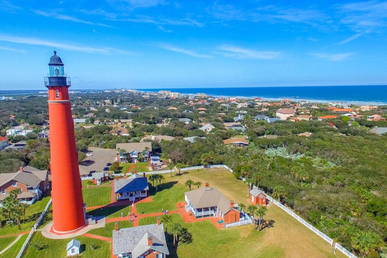 A coastal town with a prominent red lighthouse, surrounded by residential houses and lush greenery.