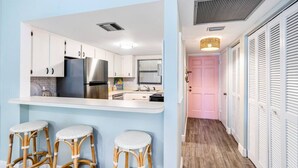 A modern kitchen with white cabinets, stainless steel appliances, and a bar area with wicker stools. - Island Time Oasis Pool Walk to Beach & Balcony (Daytona Beach)