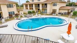 A swimming pool with lounge chairs and umbrellas, surrounded by a fence and buildings in the background. - Island Time Oasis Pool Walk to Beach & Balcony (Daytona Beach)