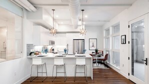 Cocina moderna con armarios blancos, una isla central con taburetes y luminarias colgantes.