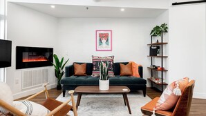 Una sala de estar moderna con un sofá verde oscuro, dos sillas de madera, una mesa de centro y un televisor montado en la pared.
