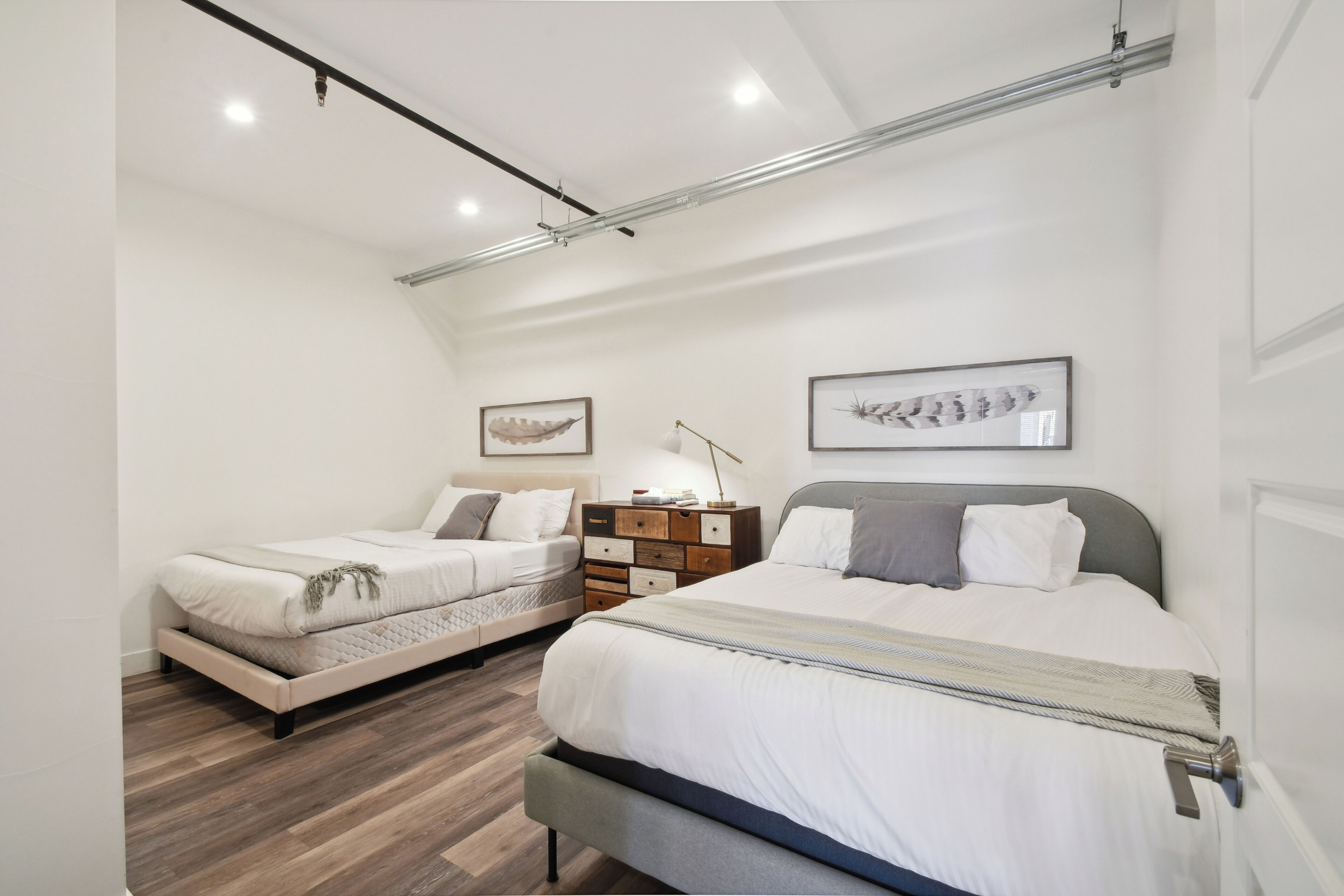 A modern bedroom with two beds, wooden flooring, and a minimalist design.