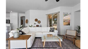 Ein modernes Wohnzimmer mit einem weißen Sofa, einem Glastisch und einem Korbstuhl.