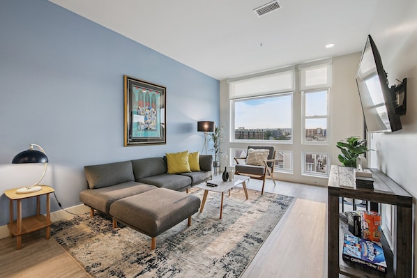 A modern living room with a grey sofa, a coffee table, and a bookshelf. - Golden Hour Designer Loft Espadin Lohi (Denver)