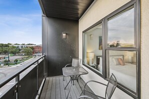 A balcony with a metal table and chairs, a view of a cityscape, and a window with a bed and lamp inside. - Golden Hour Designer Loft Espadin Lohi (Denver)