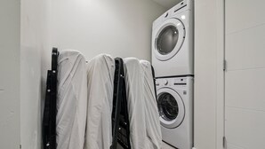 A laundry area with two stacked washing machines and a rack covered with white garments. - Golden Hour Designer Loft Espadin Lohi (Denver)