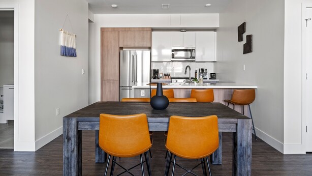 Een moderne keuken met roestvrijstalen apparatuur, een eethoek met een donker houten tafel en oranje stoelen, en een hanglamp.