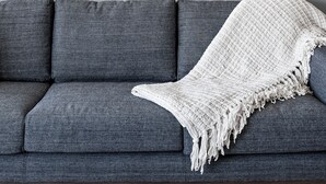 Een moderne woonkamer met een grijze bank, een witte plaid en een groot abstract kunstwerk aan de muur.