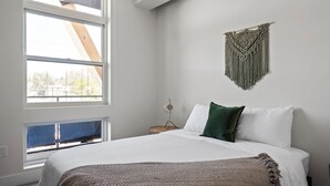 Een slaapkamer met een groot bed, een raam met uitzicht, een wanddecoratie en een nachtkastje.