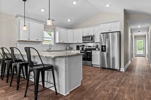 A modern kitchen with white cabinets, stainless steel appliances, and a central island with bar stools. - The 54th Cottage (Commerce)