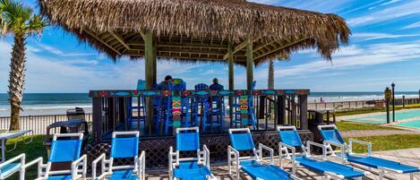 A beachside lounge with blue lounge chairs and a thatched-roof structure.