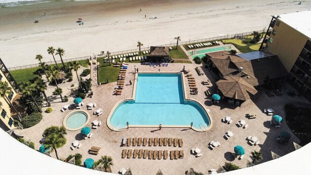 A resort with a swimming pool, beach access, and palm trees. - The Maui Wowi Oceanfront Condo (Daytona Beach Shores)
