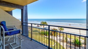 A balcony with a view of the beach, a chair, and a railing. - The Maui Wowi Oceanfront Condo (Daytona Beach Shores)