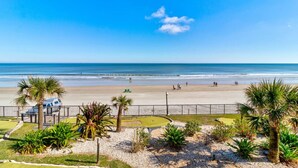 A beach with palm trees, a fenced area, and a clear blue sky. - The Maui Wowi Oceanfront Condo (Daytona Beach Shores)