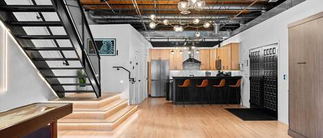 A modern kitchen with a central island, wooden flooring, and a staircase with a metal railing.