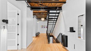 A modern interior with a wooden floor, white walls, a staircase with a metal frame, and a ceiling with exposed beams. - Suite [1] + [2] (Denver)