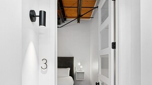 A narrow hallway leading to a bedroom with a bed, a nightstand, and a wall-mounted light fixture. - Suite [1] + [2] (Denver)