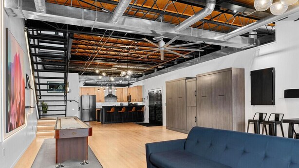 A modern interior with a blue sofa, a wooden coffee table, and a kitchen area with wooden cabinets and a black countertop. - Suite [1] + [2] (Denver)