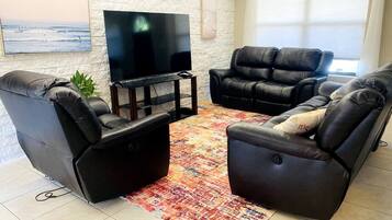 Uma sala de estar com dois poltronas de couro preto, uma televisão de tela plana e um tapete estampado.