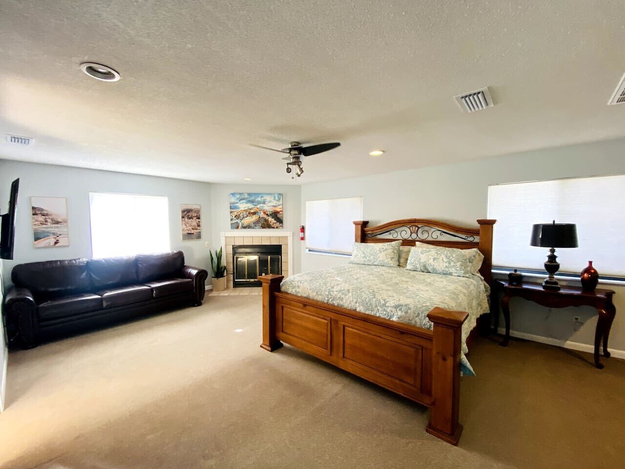 A bedroom with a wooden bed, a black leather sofa, a fireplace, and a ceiling fan.