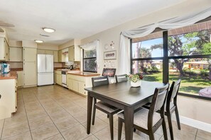 A kitchen with a dining area, large windows, and a view of the outdoors. - Sunset on the Peninsula (Daytona Beach)