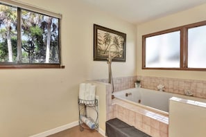 A bathroom with a bathtub, a shower, a window with a view of trees, and a towel rack. - Sunset on the Peninsula (Daytona Beach)