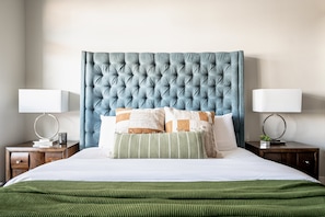 A neatly made bed with a tufted headboard, two bedside tables with lamps, and a green striped throw blanket. - 3198: Bright & Breezy at Rino Art Lofts (Denver)
