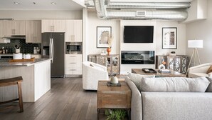 Eine moderne Küche mit Edelstahlgeräten, eine Essecke mit Holztisch und ein Wohnzimmer mit Sofa und Fernseher.
