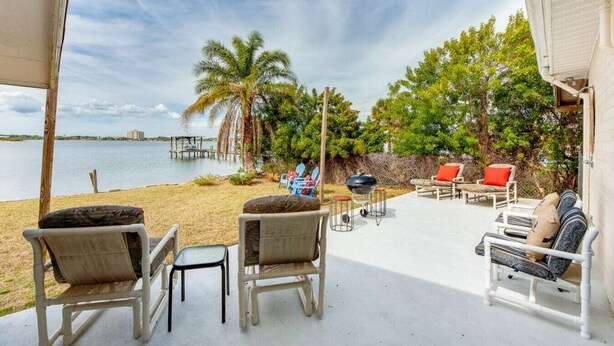 Ein Sitzbereich im Freien mit Stühlen und einem Tisch, mit Blick auf einen Strand mit Palmen und einem Pier.