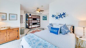 Ein Schlafzimmer mit Etagenbett, einem Bett mit blauem Kissen, einem hölzernen Schminktisch und einem Deckenventilator.