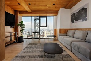 A modern living room with a large window, a grey sofa, a black ottoman, a wooden TV stand, and a potted plant. - w Charming Loft With Amazing Deco in Mexico City (Mexico City)