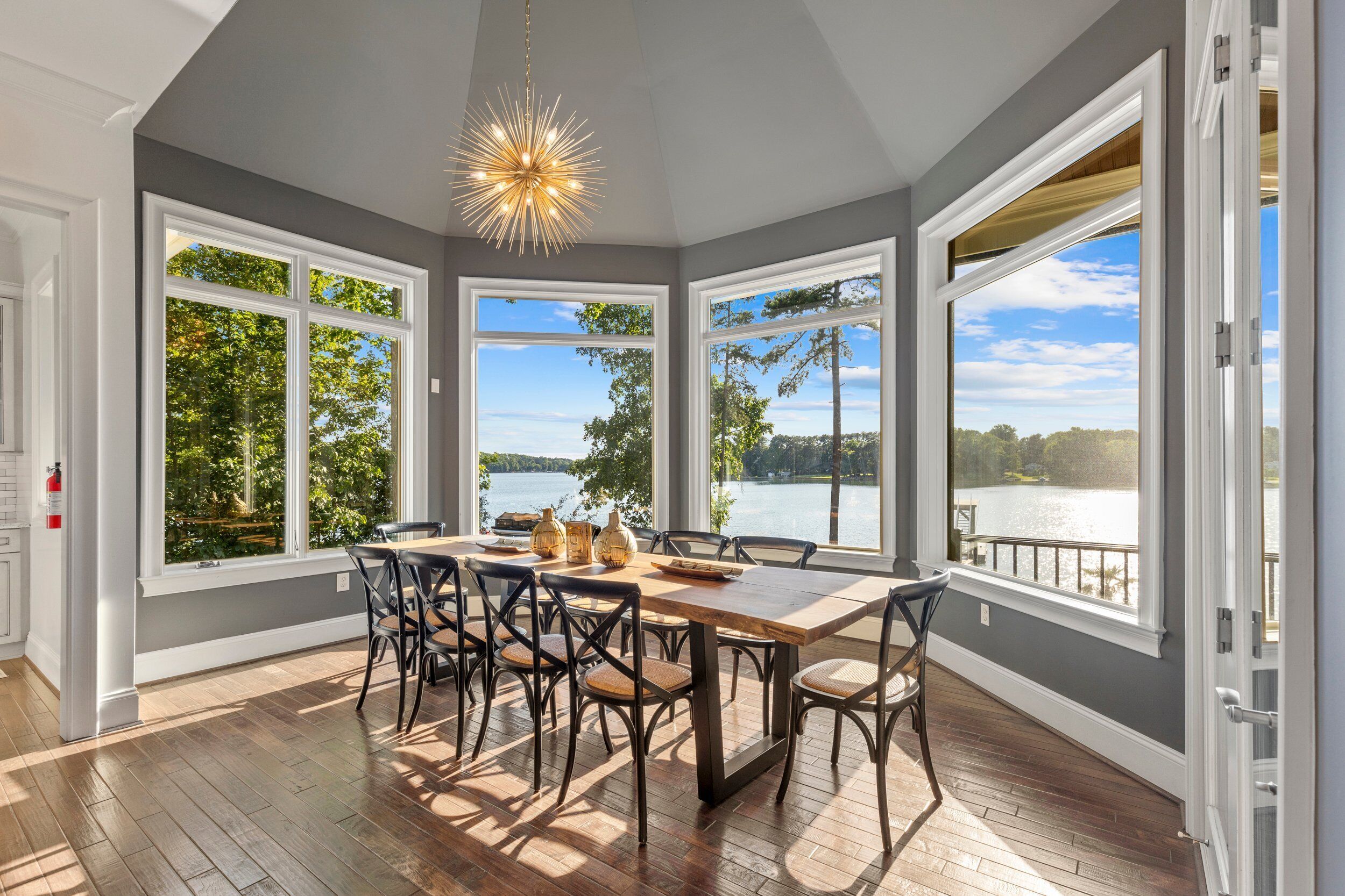 A spacious dining area with a large table and chairs, large windows with a view of a lake, and a modern chandelier.
