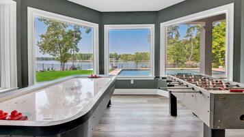 A room with a foosball table, large windows, and a view of a lake.